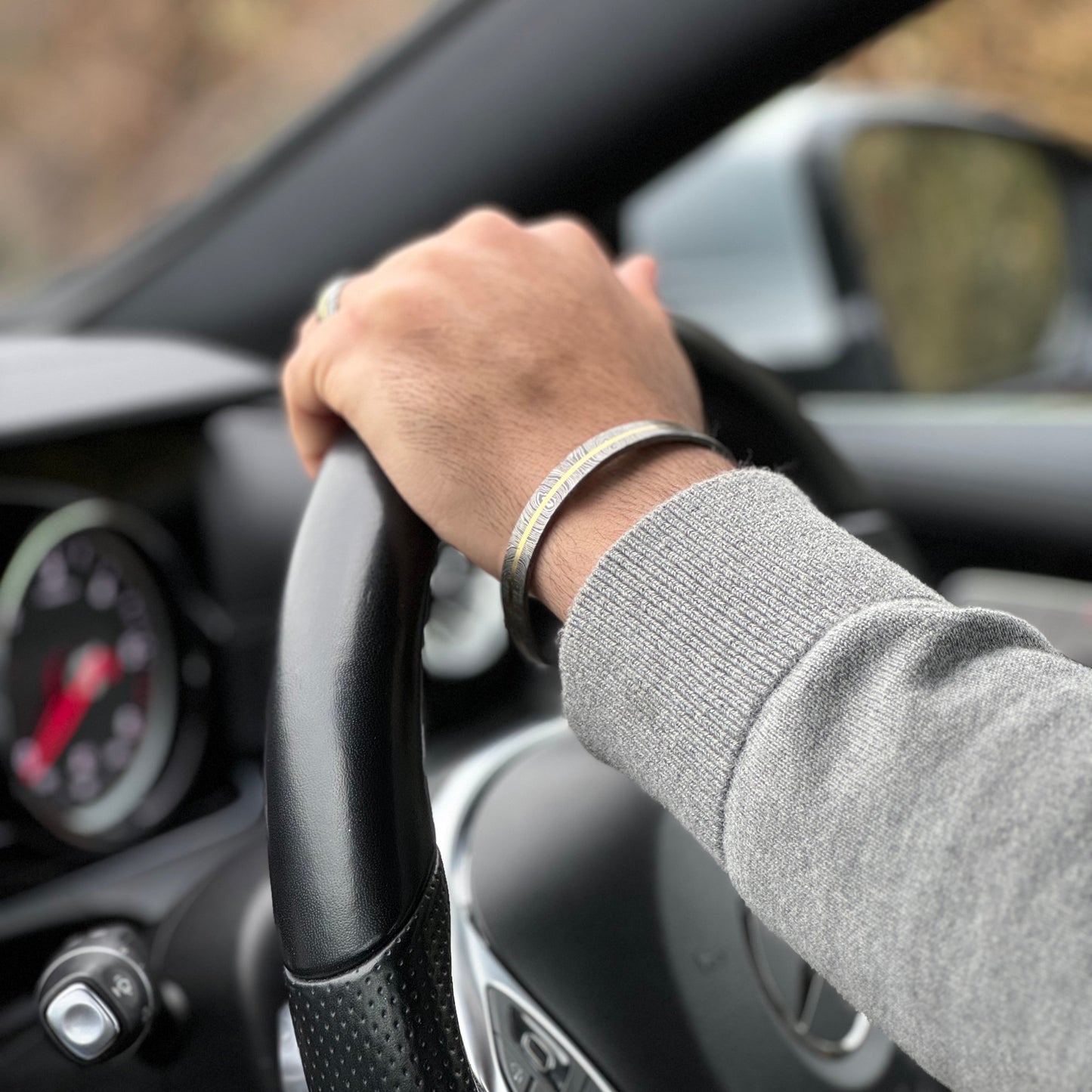 Man wearing Damascus and Brass ring and cuff driving car