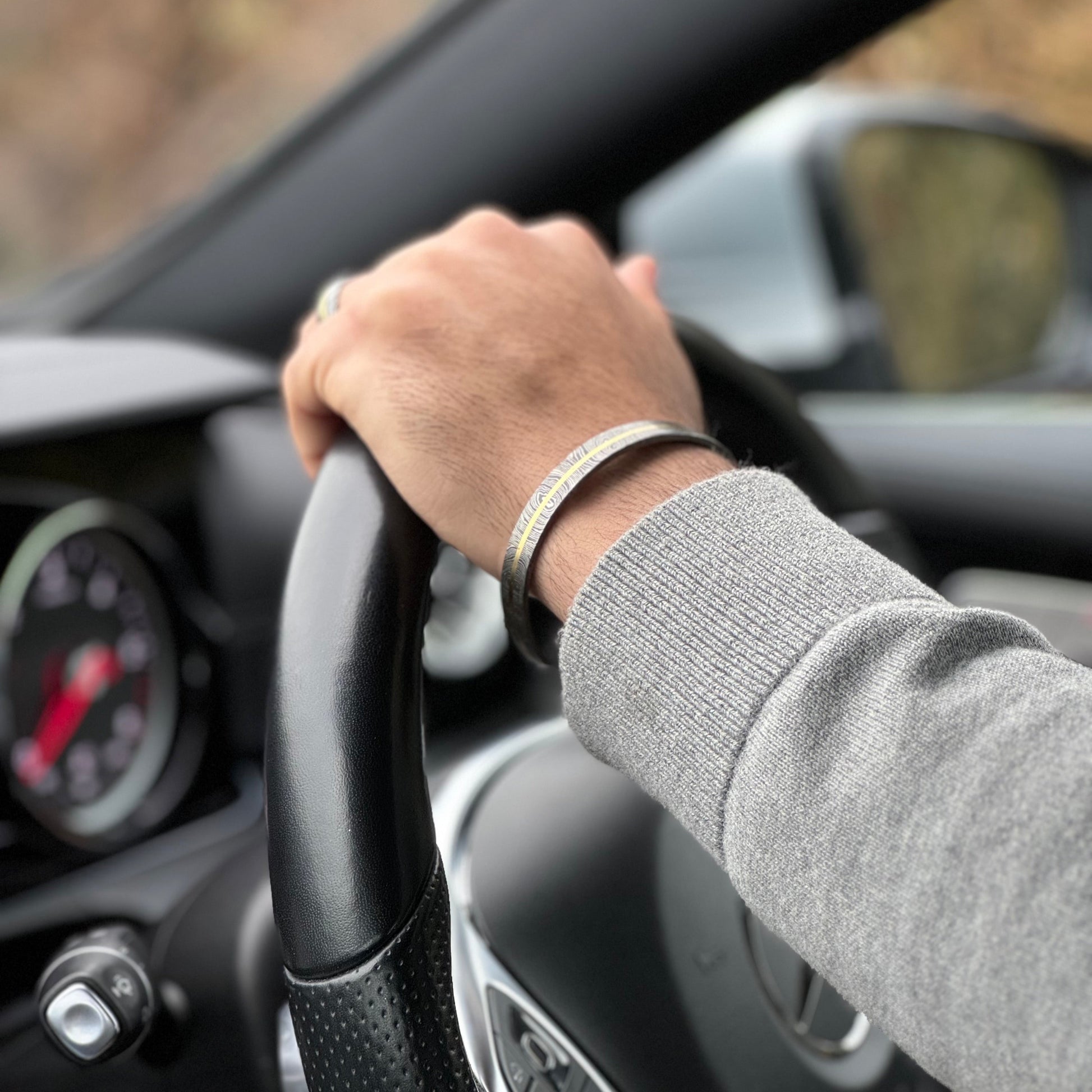 Man wearing Damascus and Brass ring and cuff driving car