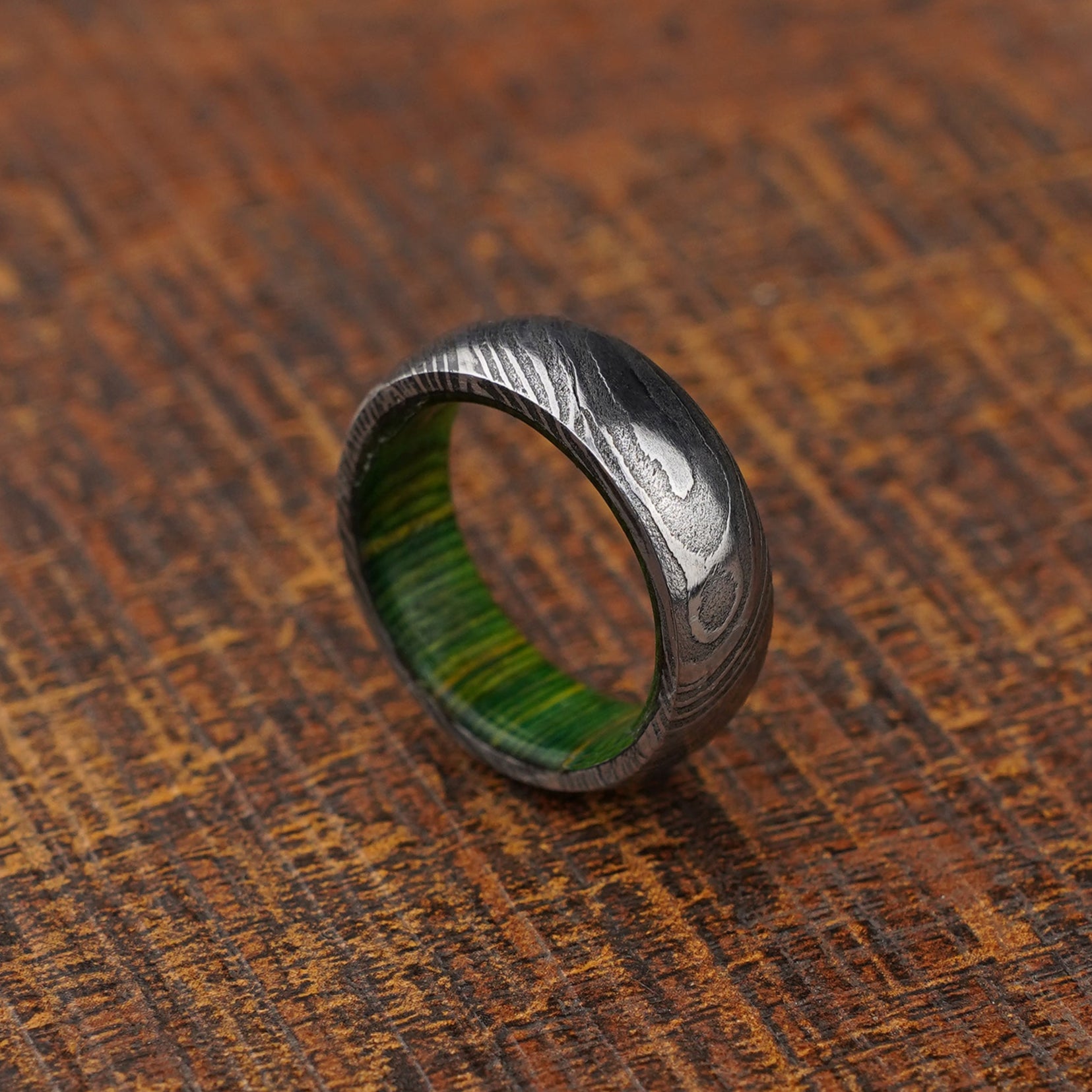 green wood inlay damascus steel ring on wooden background close up